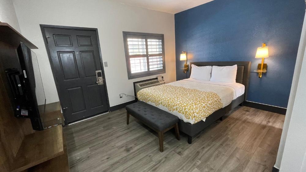 A hotel room with a bed, window, door, TV, and bench.